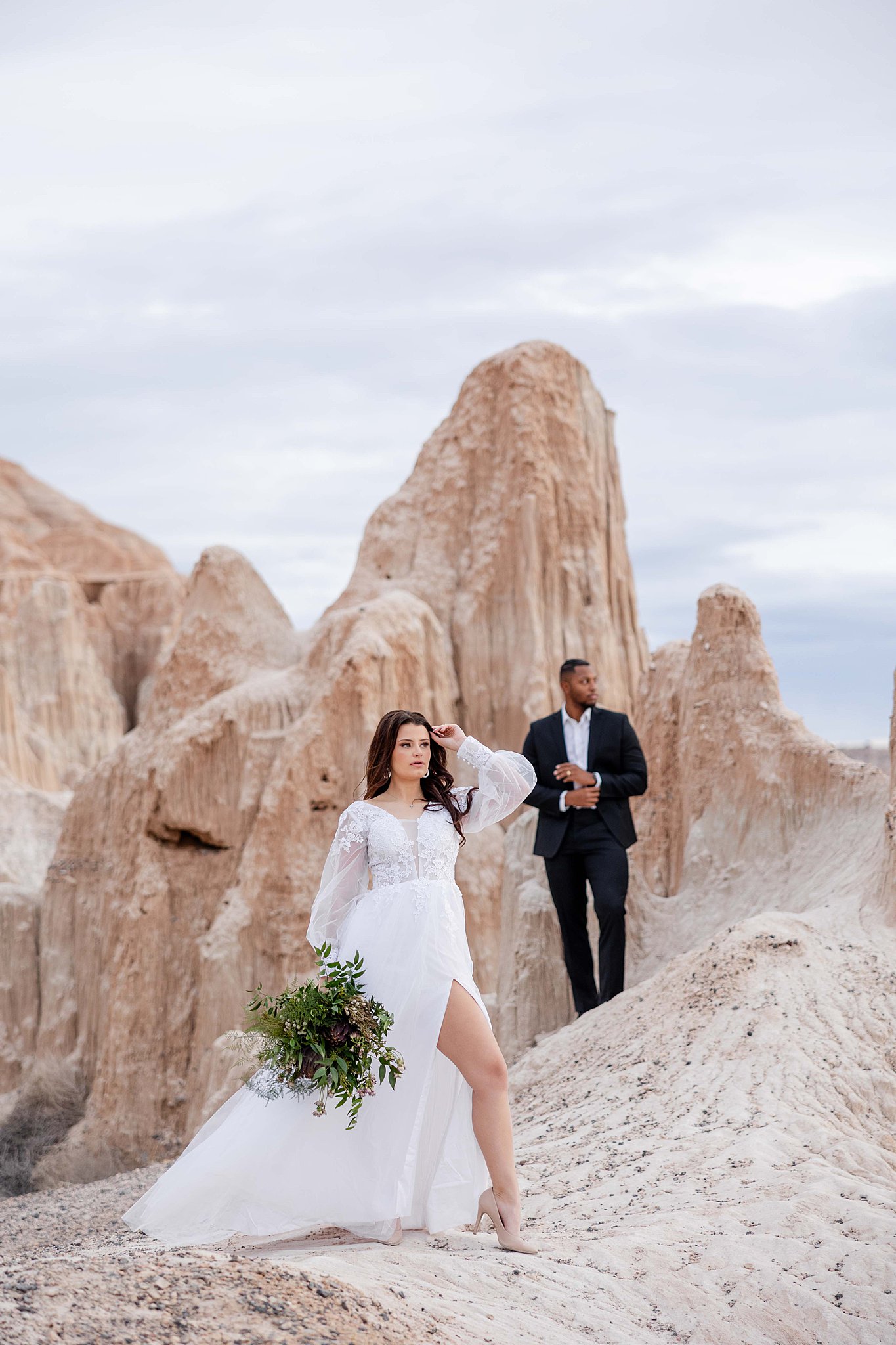 Desert elopement photo of a bride in a flowing lace wedding dress and groom in a black suit among dramatic rock formations inside the Cathedral Gorge State Park.