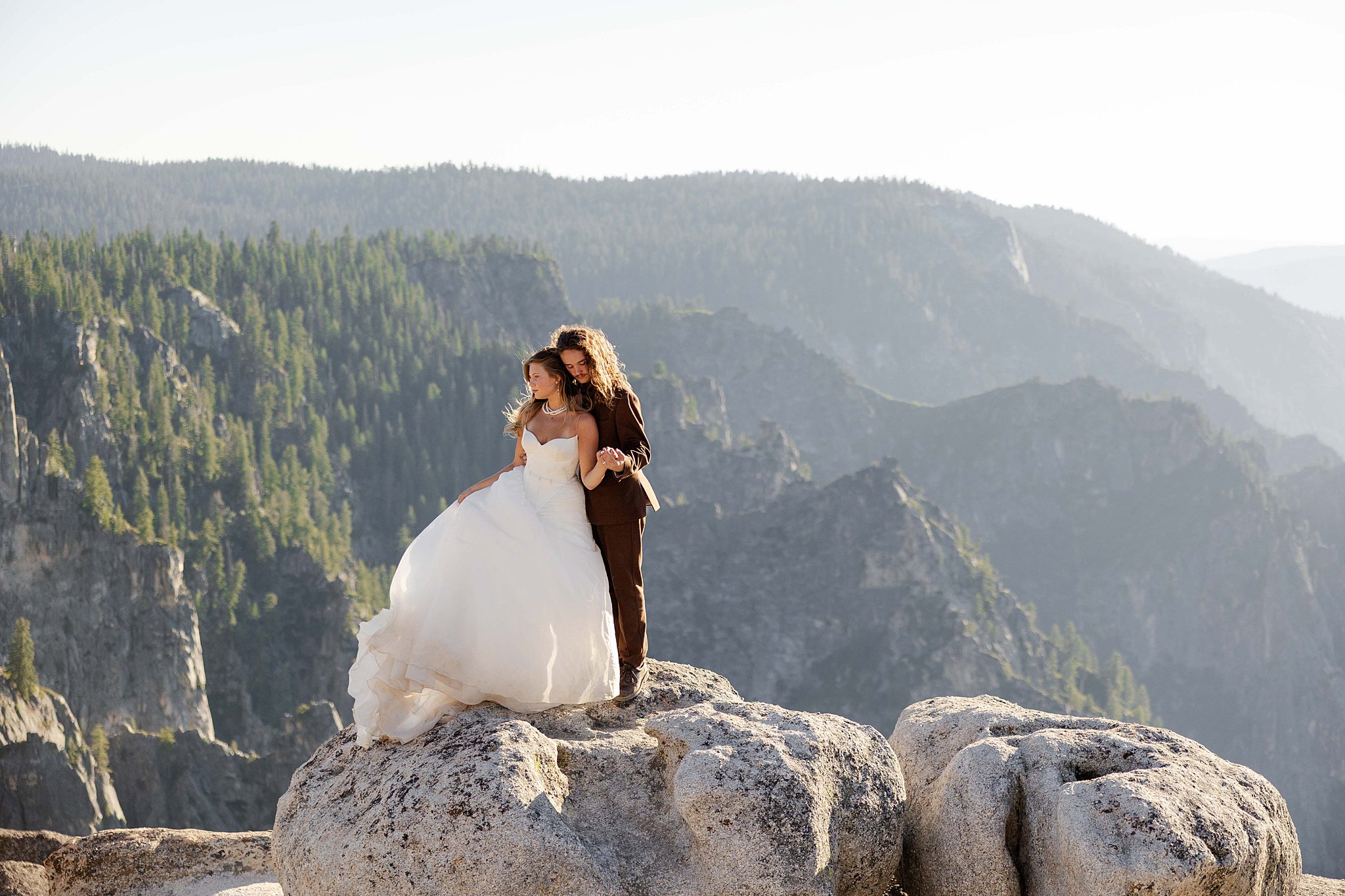 A Bride and Groom stands on the edge of Taft Point in Yosemite National Park, bathed in golden sunset light above a dramatic canyon.