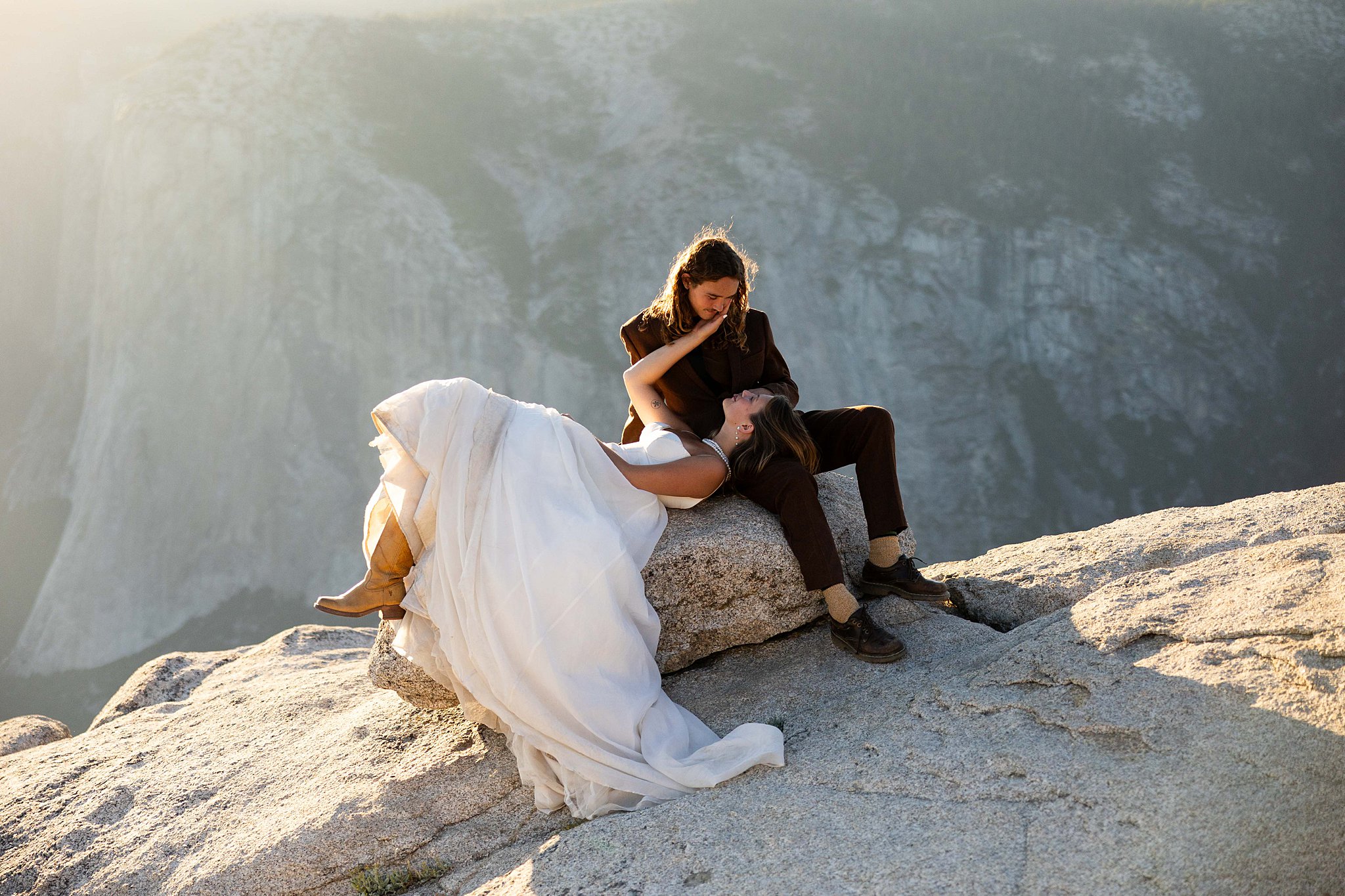 A Bride and Groom stands on the edge of Taft Point in Yosemite National Park, bathed in golden sunset light above a dramatic canyon.