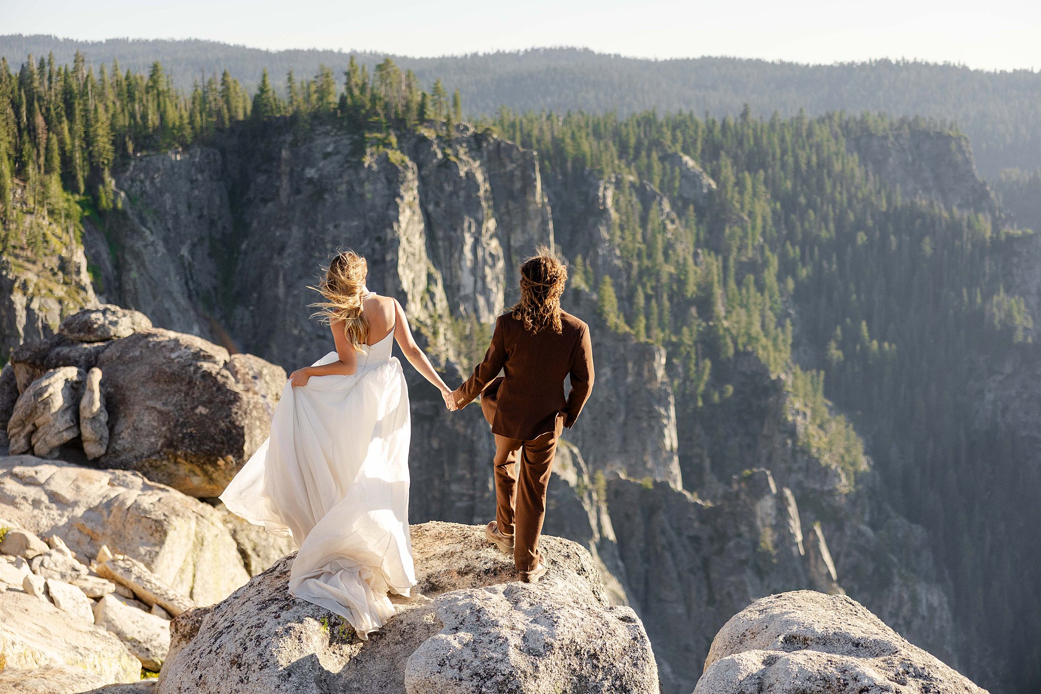 A Bride and Groom stands on the edge of Taft Point in Yosemite National Park, bathed in golden sunset light above a dramatic canyon.