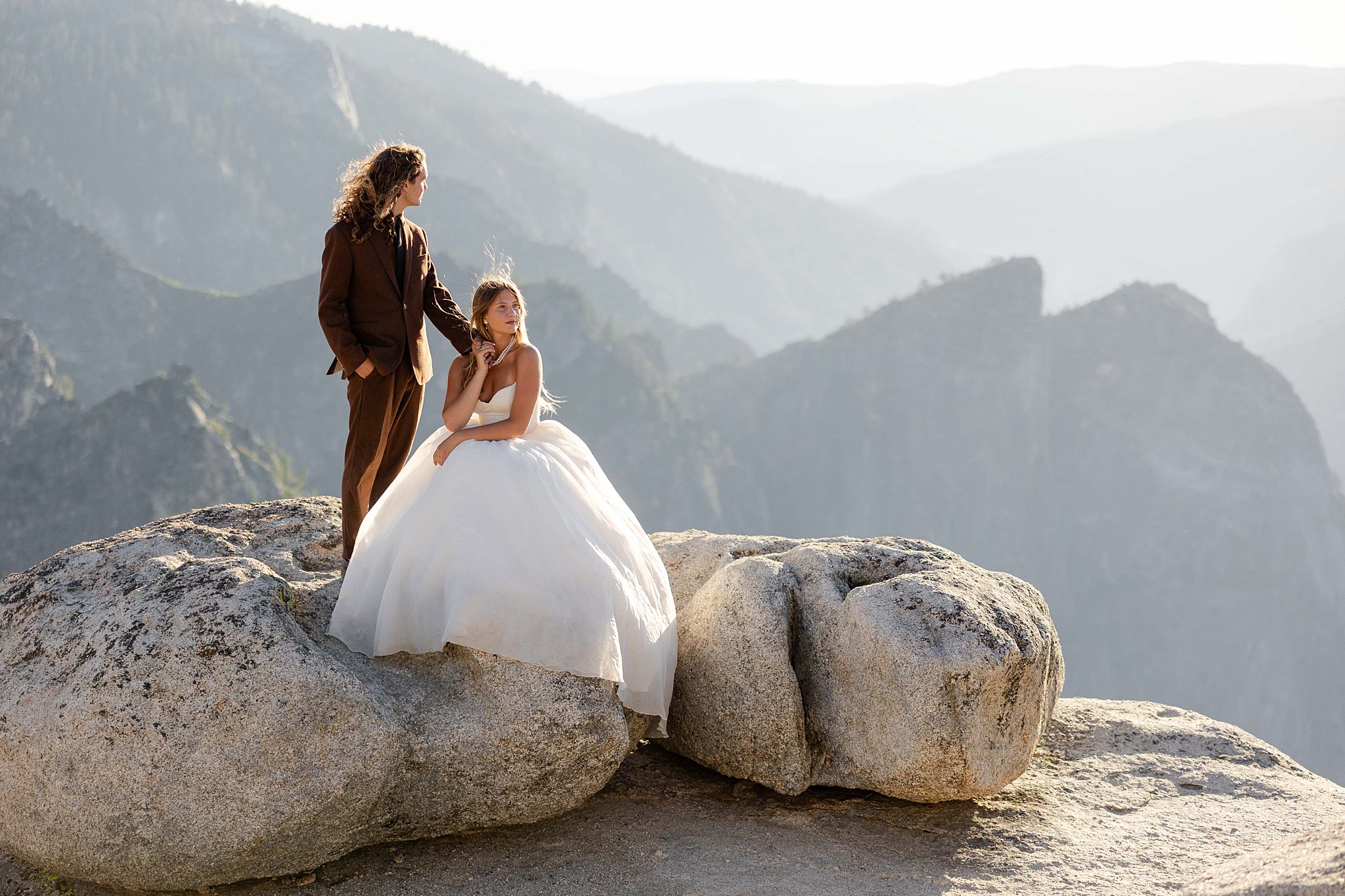 A Bride and Groom stands on the edge of Taft Point in Yosemite National Park, bathed in golden sunset light above a dramatic canyon.
